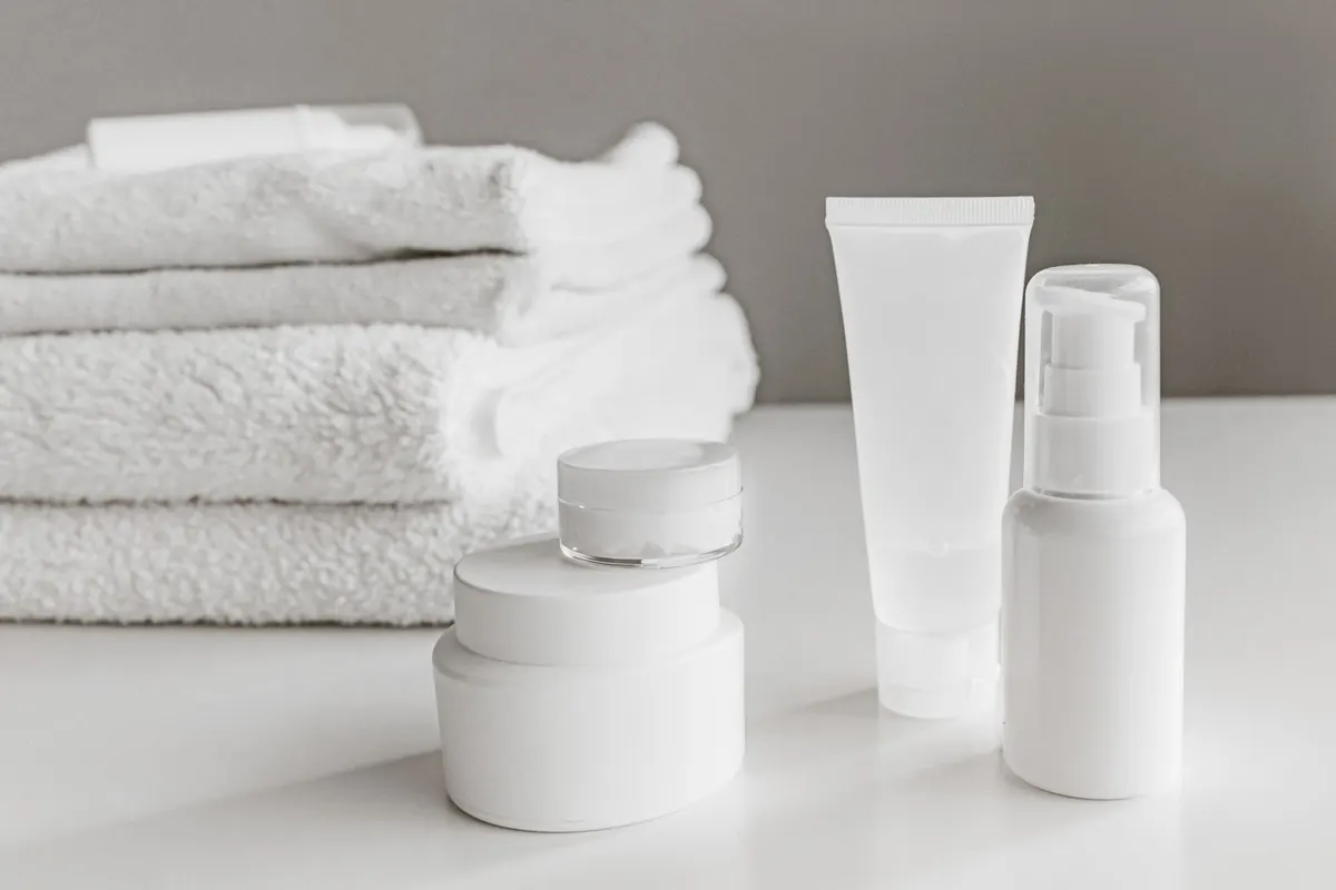 Folded white towels and unbranded skincare jars on a pale surface