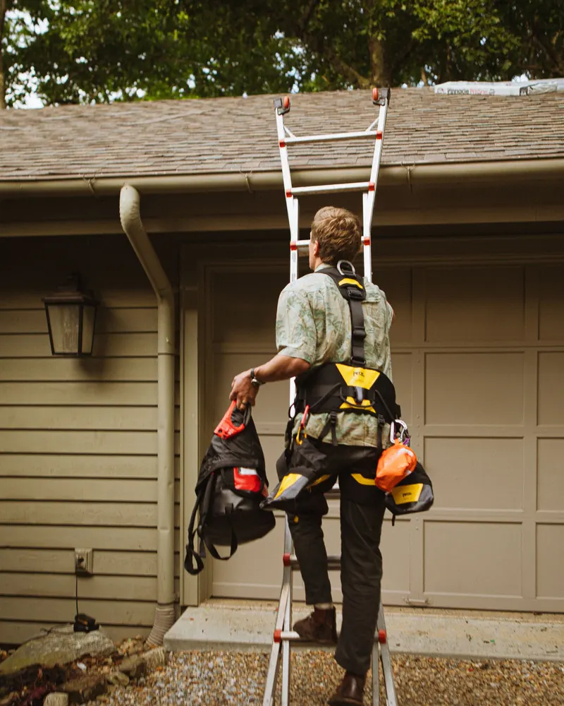 Roofer with a tool belt climbing a ladder to the roofline