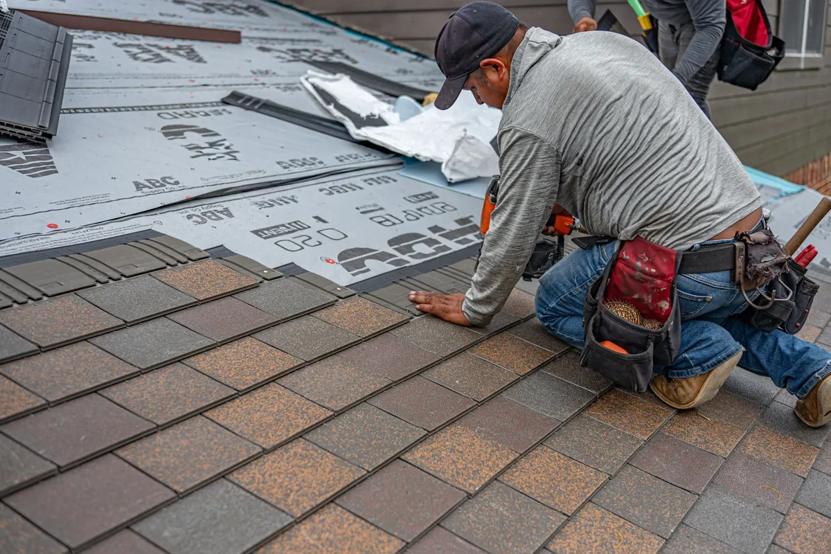 Roofer kneeling on a roof installing new asphalt shingles